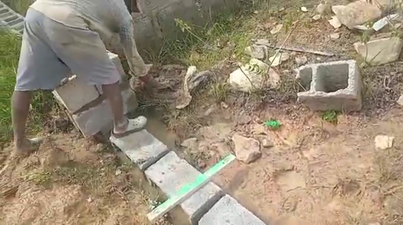 A mason laying a hollow block course to a line on a boundary wall in New Karu