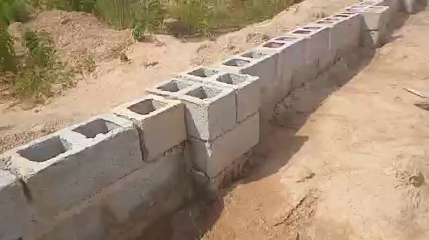 Blockwork boundary wall with hollow-block columns running alongside a site road, New Karu