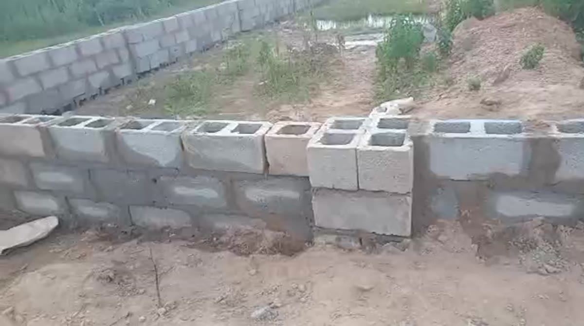 Hollow block courses laid over a wall, with open ground and water beyond